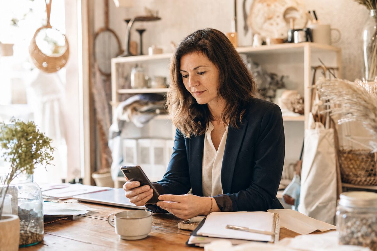 A small business owner checking their Google search results on a smartphone at a wooden desk, warm morning light, independent shop setting