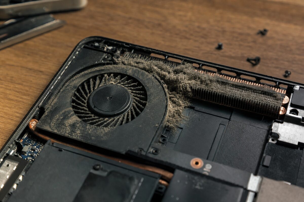 A laptop opened on a workbench with visible dust buildup around the cooling fan and heatsink fins