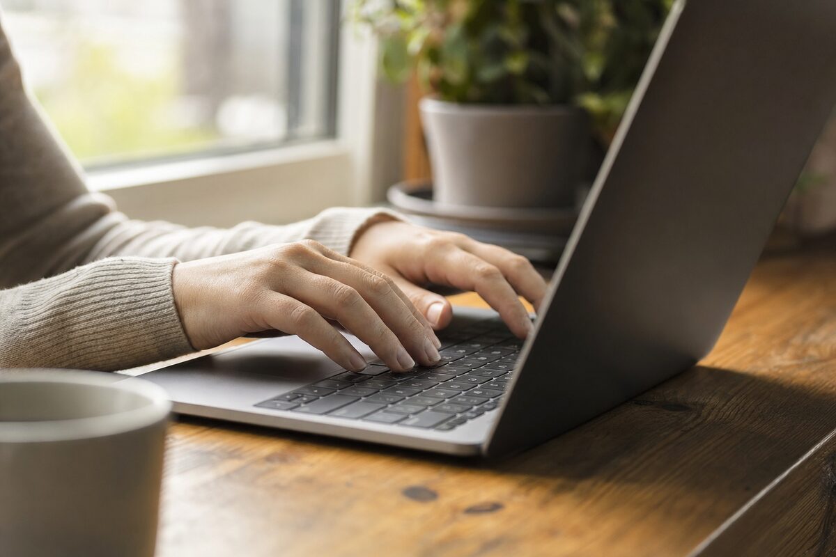 Close-up of a laptop keyboard with fingers mid-type, soft natural window light, slightly warm tone