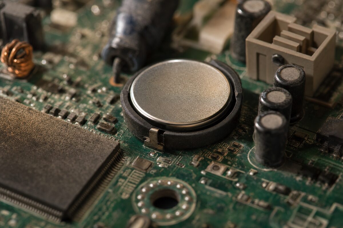 A small silver CR2032 coin cell battery resting on a computer motherboard, lit with warm workshop lighting